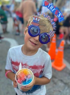 Child dressed in patriotic clothes and glasses enjoying his Snowie shaved ice at fireworks