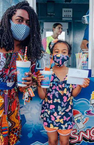 Mother and child holding cups of shaved ice in front of Snowie trailer
